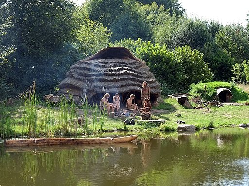 Menschen sitzen am Ufer eines kelinen Sees vor dem Mesolithikum