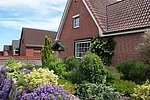 Im Vordergrund ist ein Garten mit unten Blumen zu sehen. Das Haus ist ein Backsteinhaus